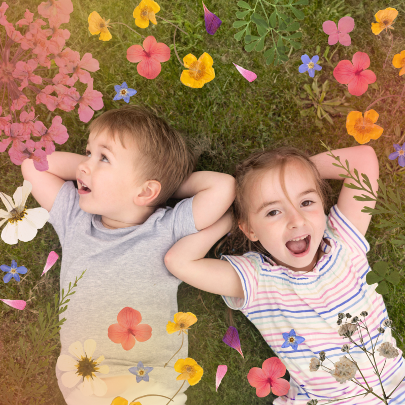 Photo of two kids lying on green grass, decorated with a spring flower overlay featuring bright blooms, leaves, and floating petals.